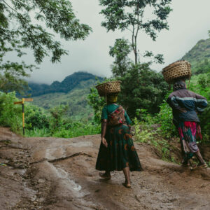 local women walking a muddy path in a lush, rural area of Tanzania