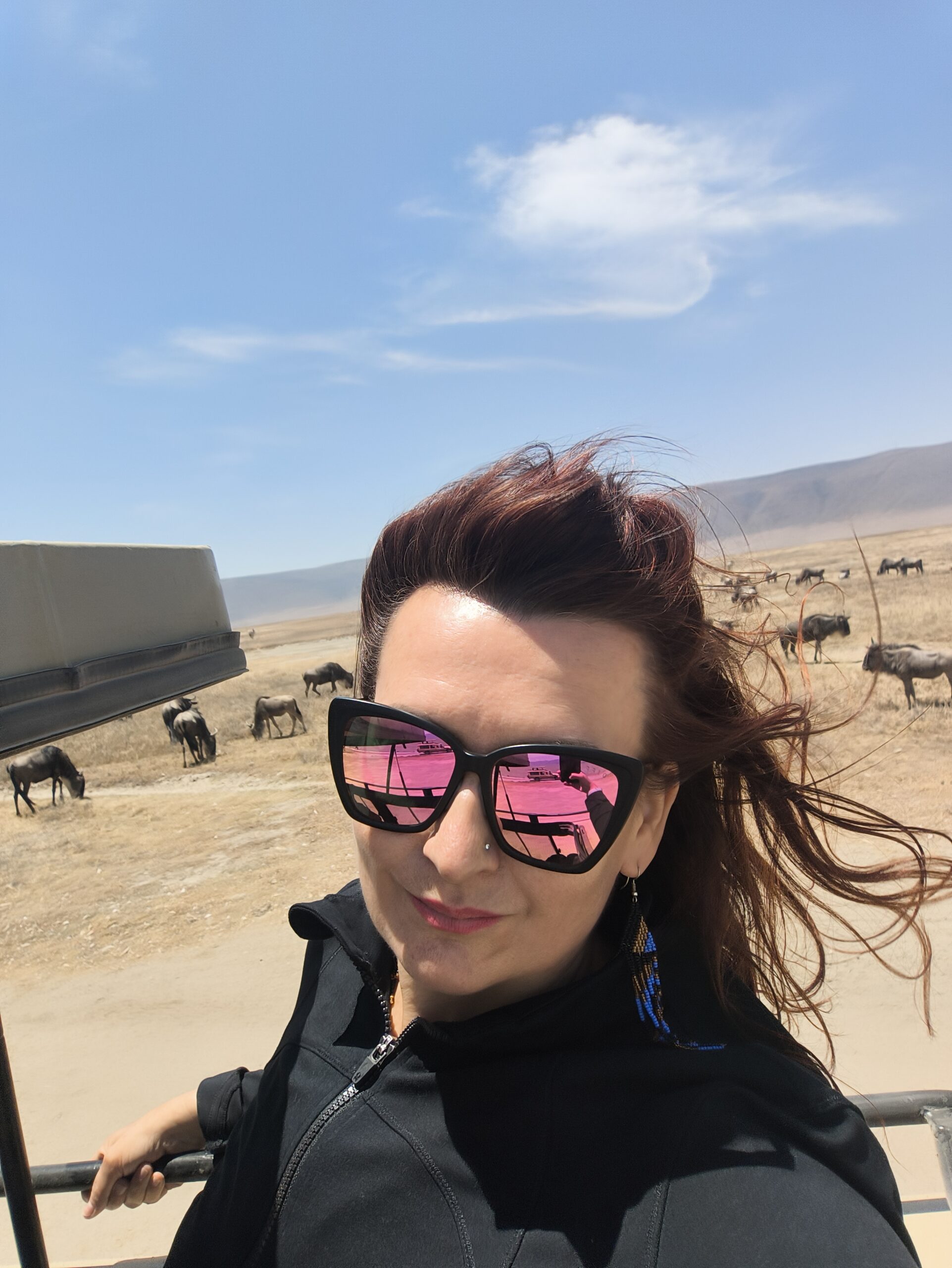 Kobieta na safari w kraterze Ngorongoro, w tle stado gnu na sawannie